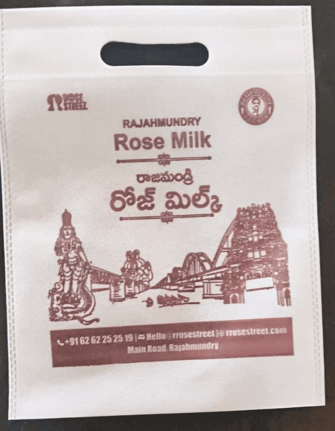 Non-woven D-cut bag for Rajahmundry Rose Milk with bilingual print and city skyline